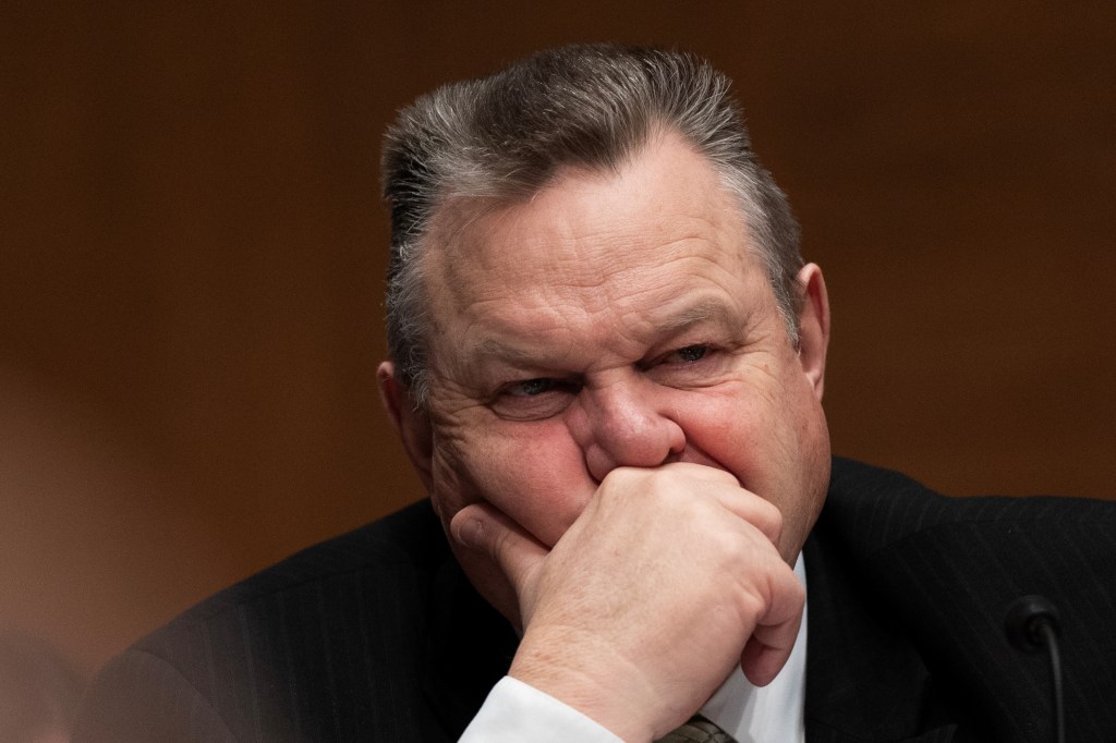 U.S. Senator Jon Tester in a suit, listening intently at a Senate Banking, Housing, and Urban Affairs Committee hearing ahead of Jerome Powell's testimony