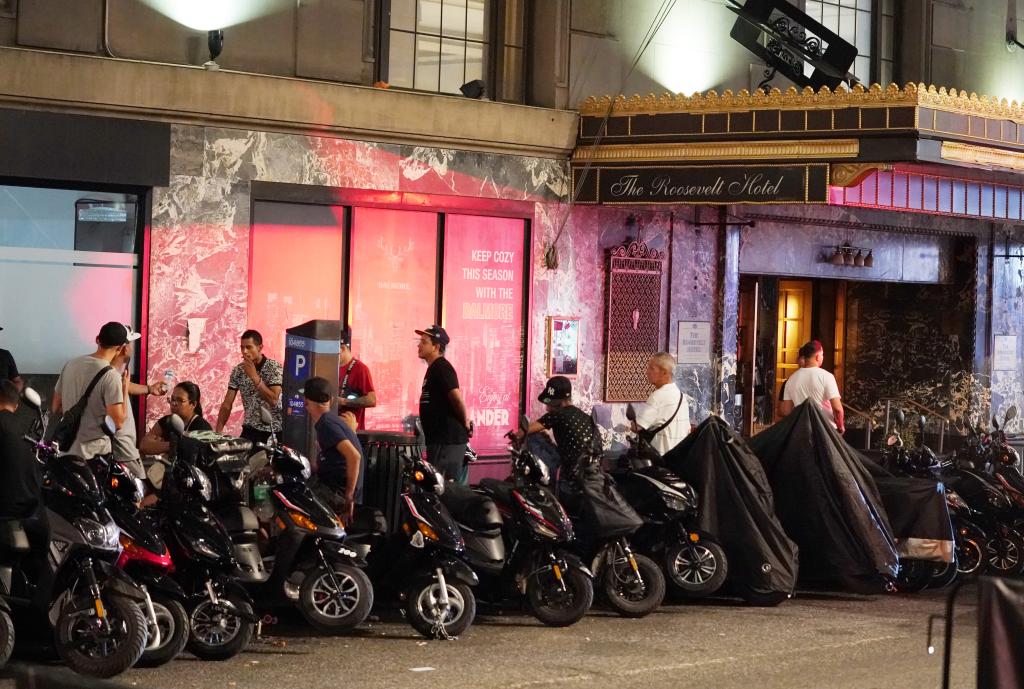 Migrants and scooters outside the Roosevelt Hotel in New York, with NYPD removing unregistered or illegally parked vehicles