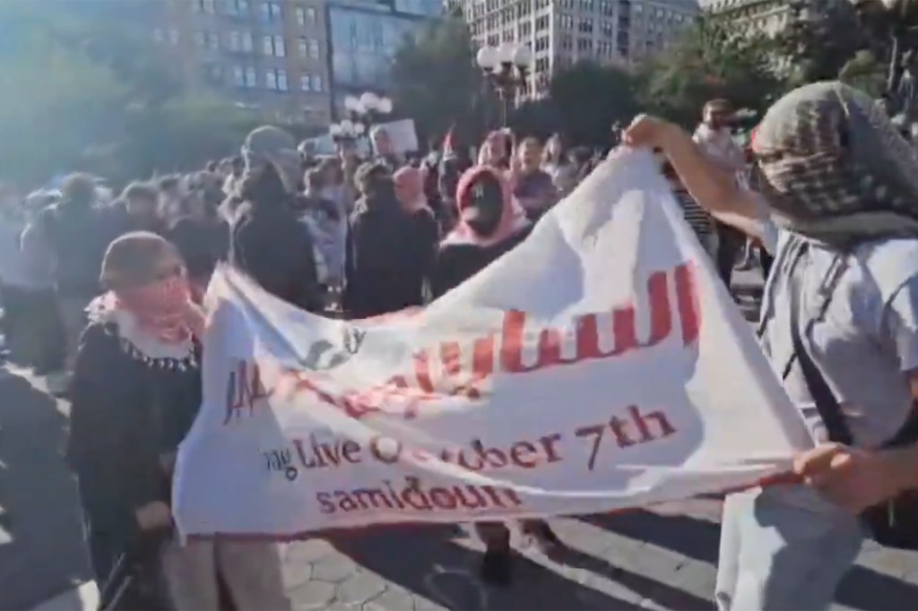 Anti-Israel protesters marching with a flag that says "Long Live October 7th" outside Nova festival exhibit.