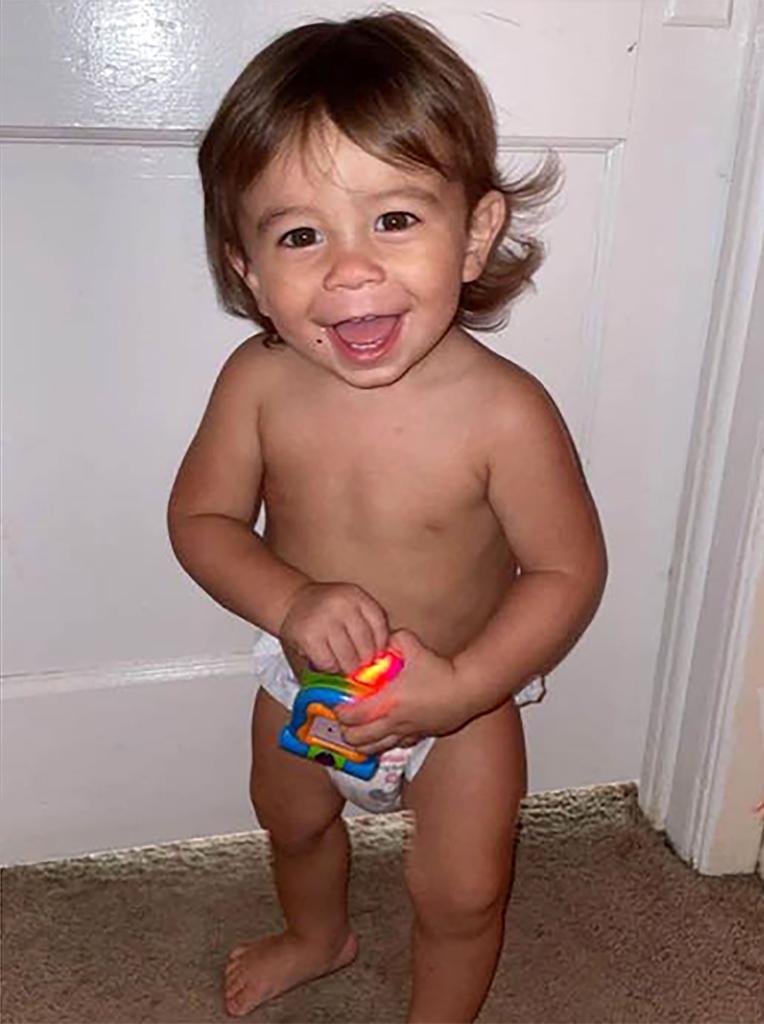 Quinton Simon stands up wearing a diaper and holding a toy while smiling