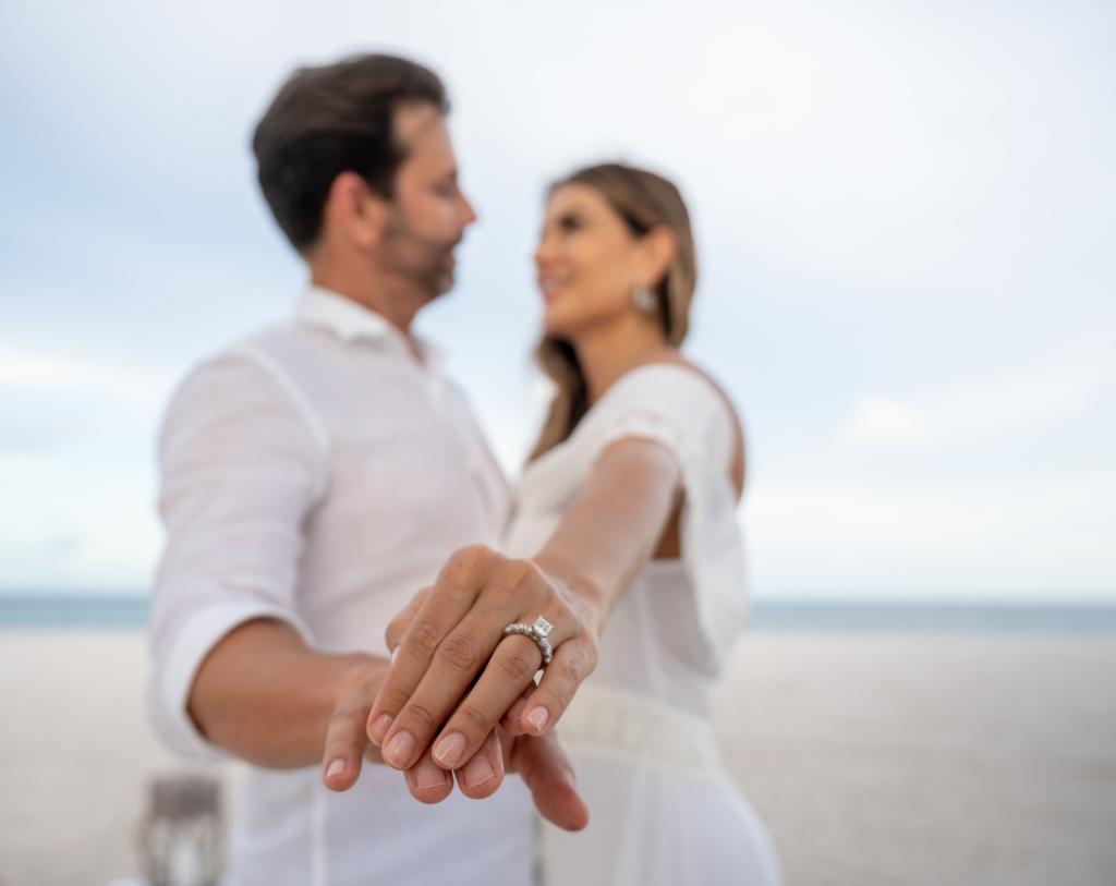 A couple showing their engagement ring to the camera while standing on a beach