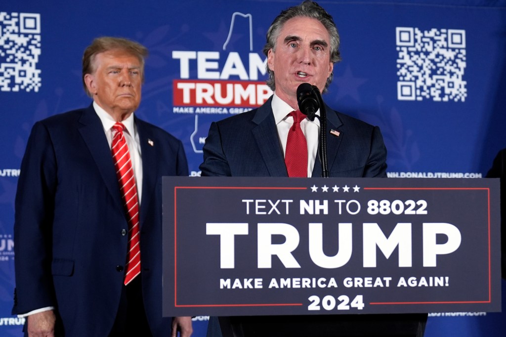 Former President Donald Trump listening to North Dakota Governor Doug Burgum speak at a campaign event on stage in Laconia, N.H., 2024
