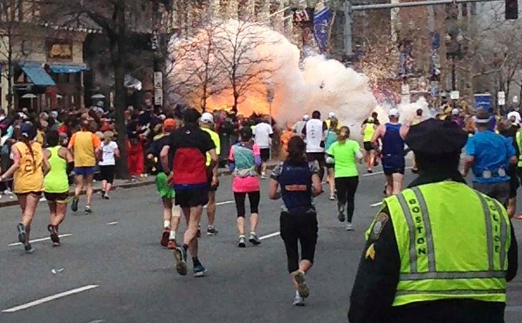 Runners continue to run towards the finish line of the Boston Marathon as an explosion erupts as a result of a terrorist bombing.