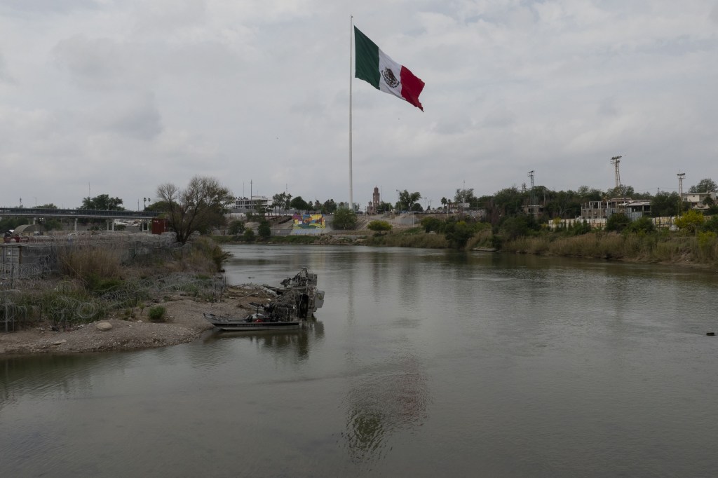 A Mexican flag seen waving on a tall flagpole from the US side of the Rio Grande river in Eagle Pass, Texas