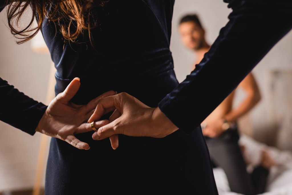 woman with hands behind back taking off wedding ring with man nearrby