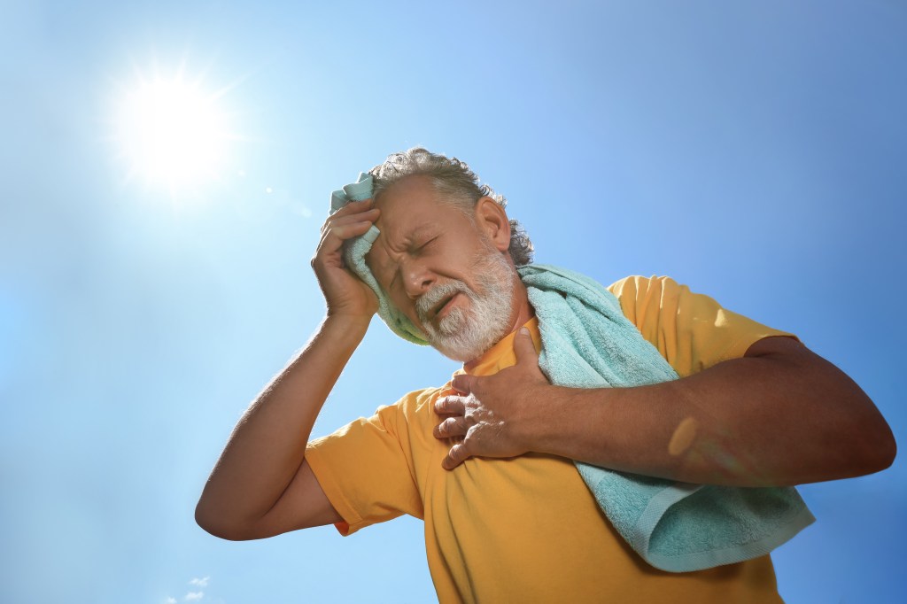 Senior man with towel suffering from heat stroke outdoors, low angle view