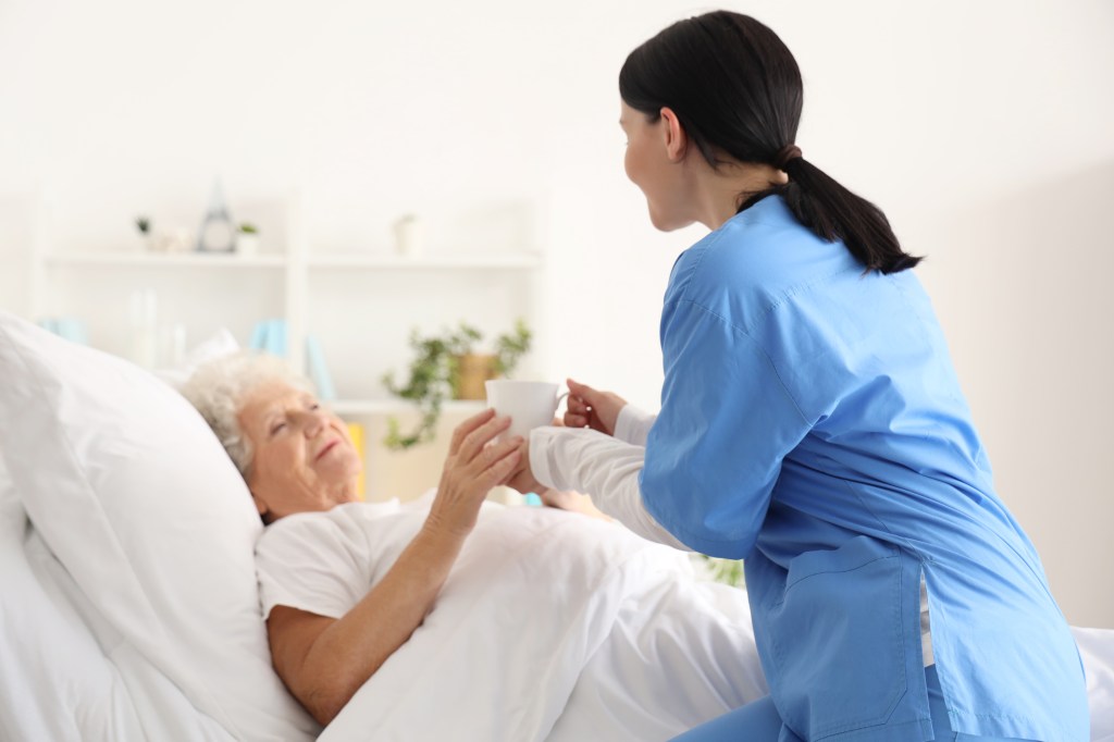 Nurse handing over a cup of tea to a senior woman in a bedroom