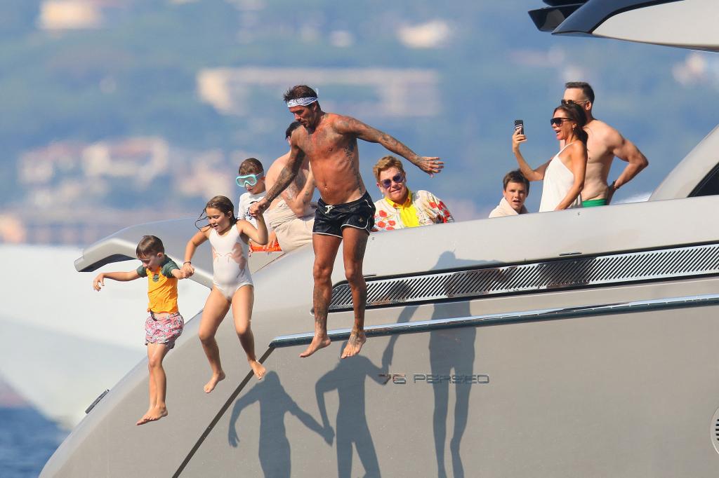 David Beckham shirtless, holding hands with his child and a child of Elton John, jumping off a yacht, with Victoria Beckham, Elton John and David Furnish watching, in southern France.