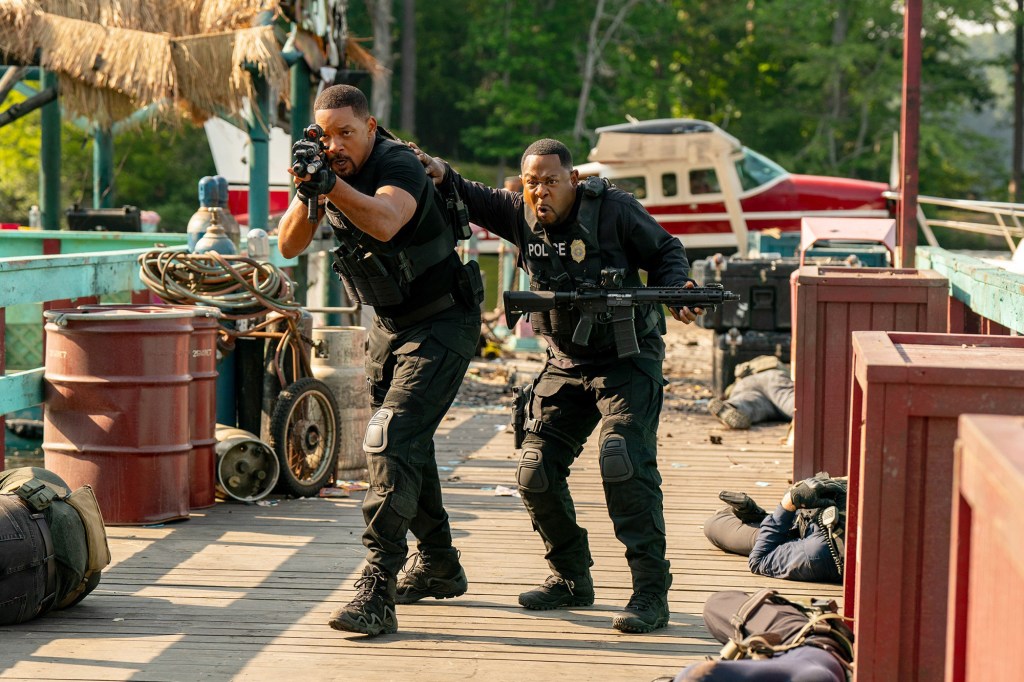 A scene from “Bad Boys: Ride or Die,” shows stars Will Smith and Martin Lawrence dressed as police officers carrying long guns through a marina.