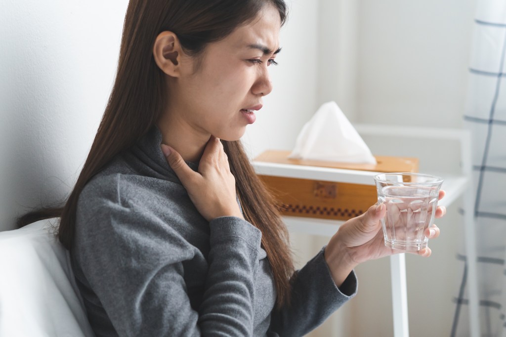 Sore throat in flu season. Young asian woman touching her neck and feeling pain in throat in the bedroom at home.