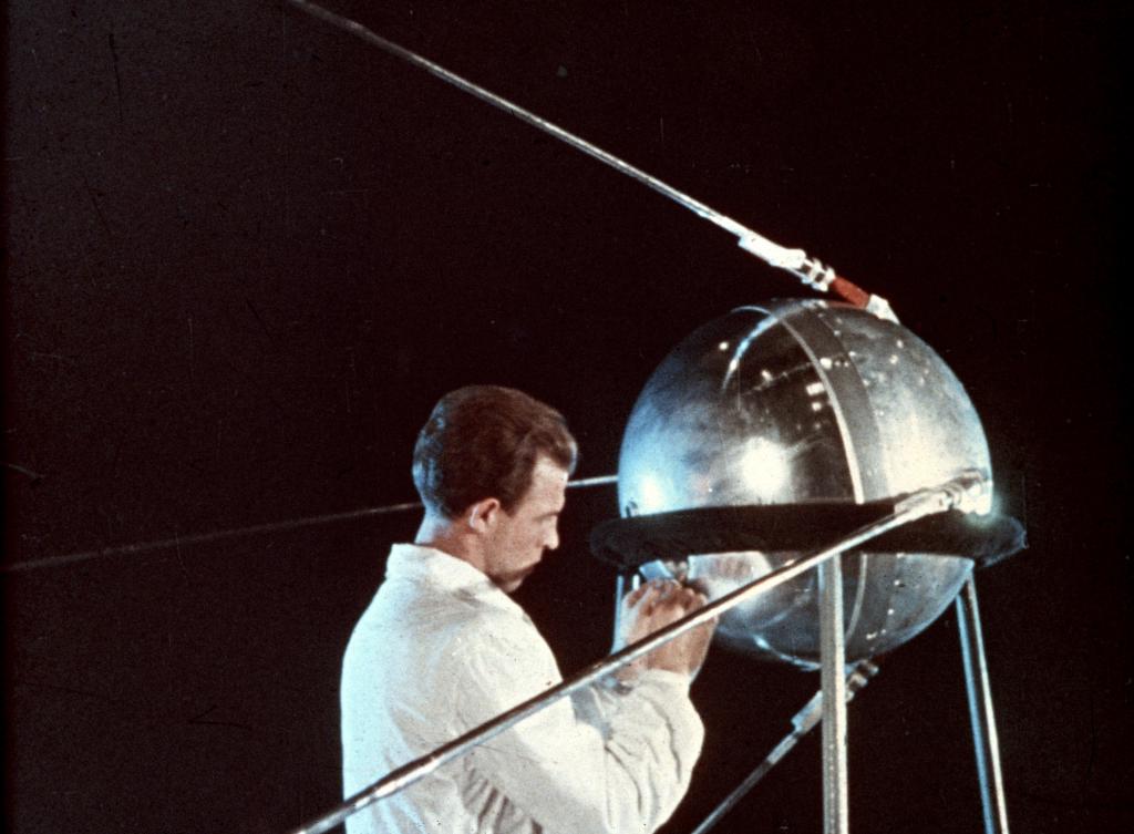 A scientist in white coat tinkers with the Sputnik salary, against a black background. 
