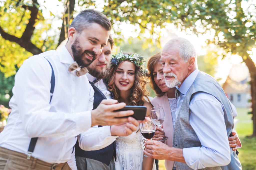 Bride, groom, and wedding guests taking a group selfie outside during the reception