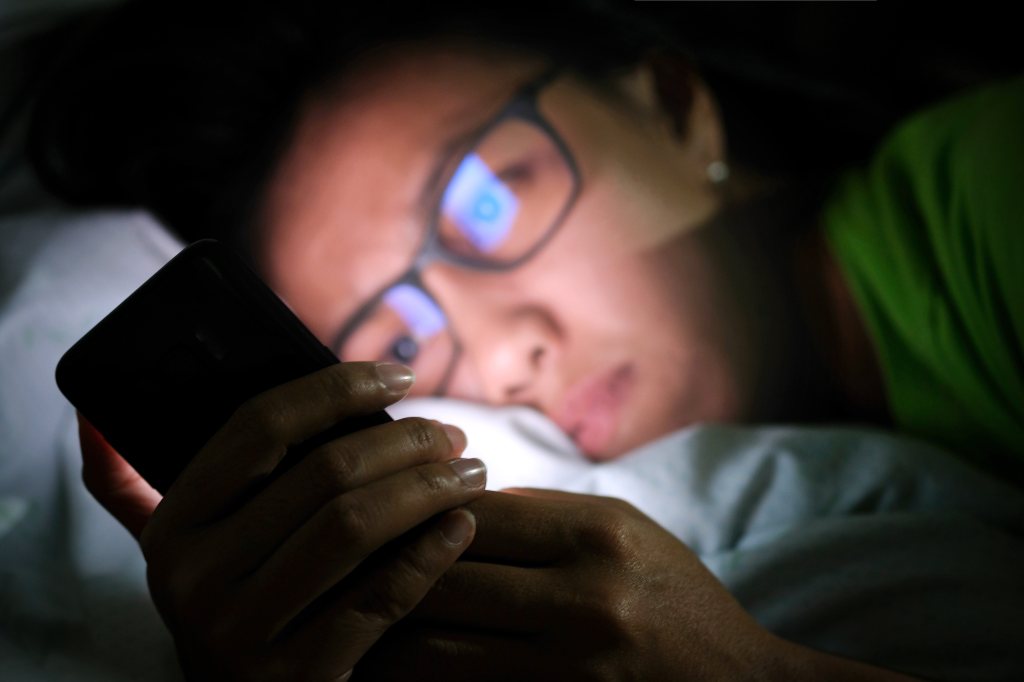 A member of Gen Alpha is seen scrolling on a smartphone emitting blue light.