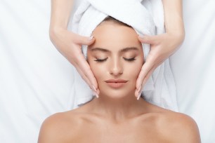 Young girl with thick eyebrows and perfect skin receiving a face massage, towel on head, spa and skincare concept.