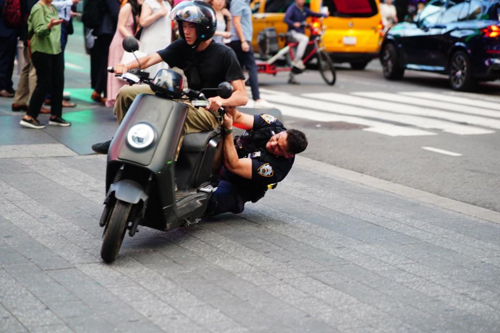 Police officer seizing an unregistered moped in Times Square while arresting a reckless driver who attempted to flee, causing minor injuries to the officer