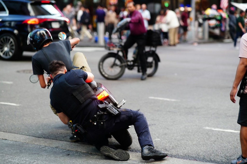 A photo of an officer struggling with a moped/motorcycle rider