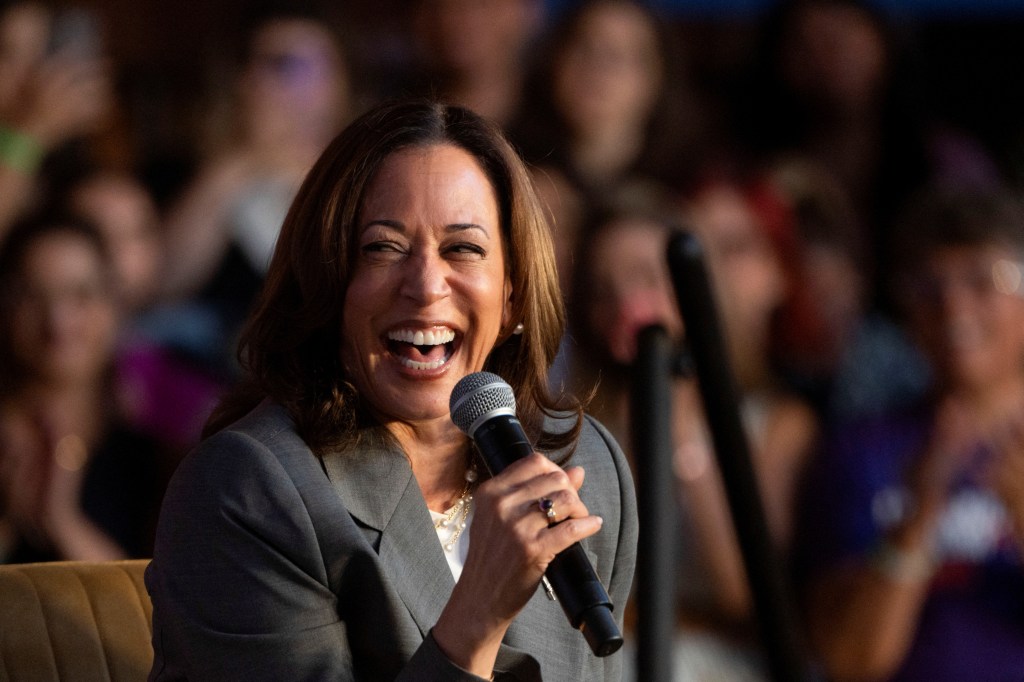 kamala harris laughs while holding a microphone