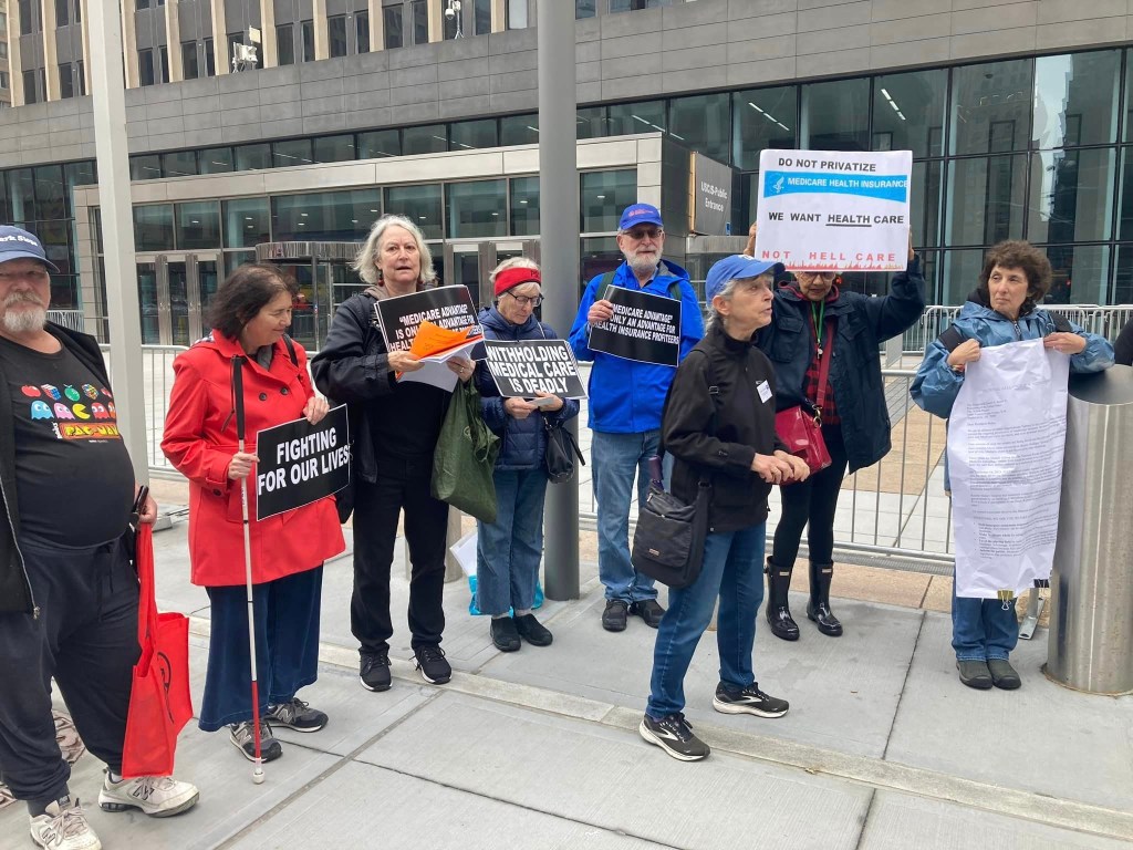 Group of UFT retirees holding signs in protest over Medicare coverage, including Kathleen Kuhfuß