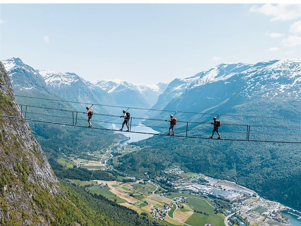 A group of people walking on a high rope course, Via Ferrata Loen, above a scenic fjord landscape in Norway