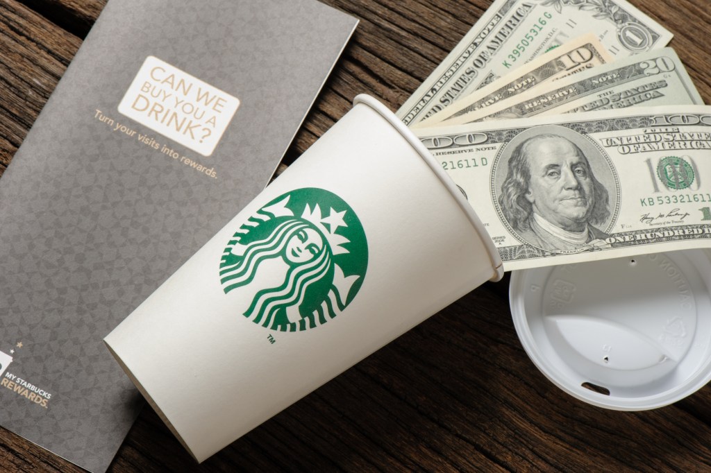 White paper cup with Starbucks logo and Dollar bills.