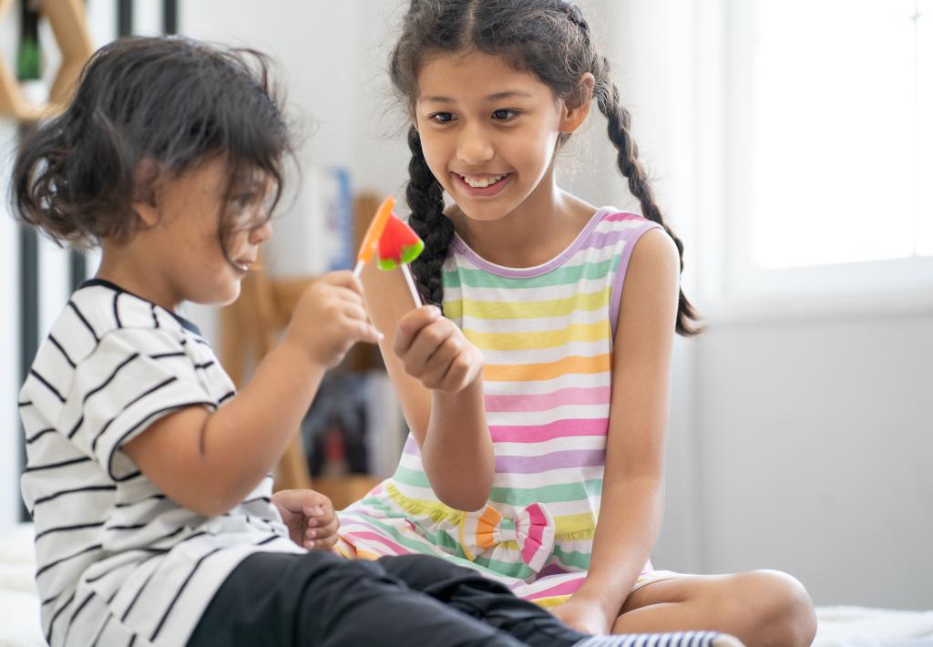 Young girl and little boy happily eating sweet candy