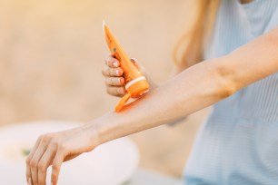 Young woman applying sunscreen on her hands while lying on a sunbed at the beach during summer holiday