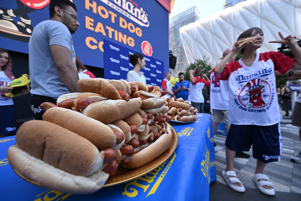 Miki Sudo, Nick Wehry, and Yuka Kinoshita at Nathan's Famous Fourth of July International Hot Dog Eating Championship Weigh-In event, standing next to a table full of hot dogs.