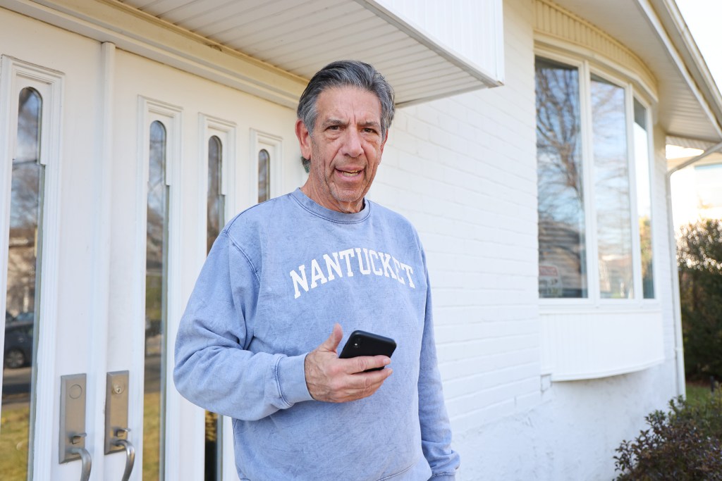 Barry Pollack standing outside his home at 31 Friendly Lane, Jericho, NY, holding a phone