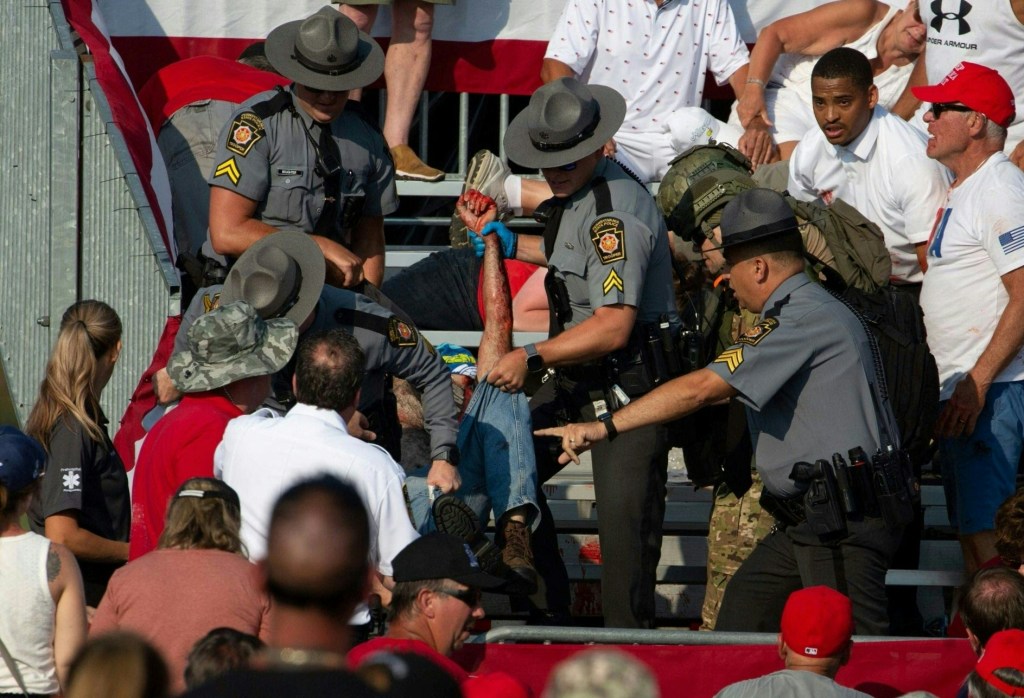 A person being removed by police officers from the stands after shots were fired at Trump.