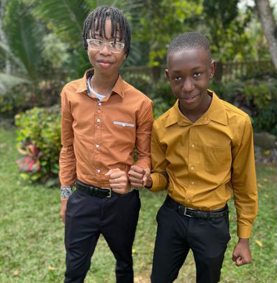 Tavayne Weir and D'andre Graham stand next to each other outside, wearing black pants and an orange and mustard shirt, respectively, smile and fist-bump