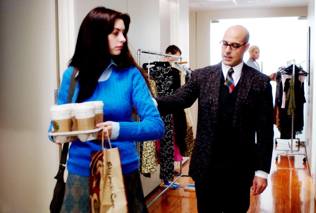 Anne Hathaway carrying a tray of coffee and bags with Stanley Tucci in the background, from the film 'The Devil Wears Prada', 2006.