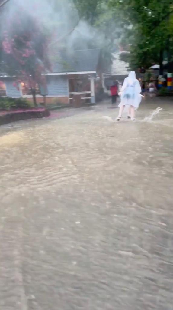 A person in a raincoat running through a flooded Dollywood theme park during heavy rain in Pigeon Forge, Tennessee