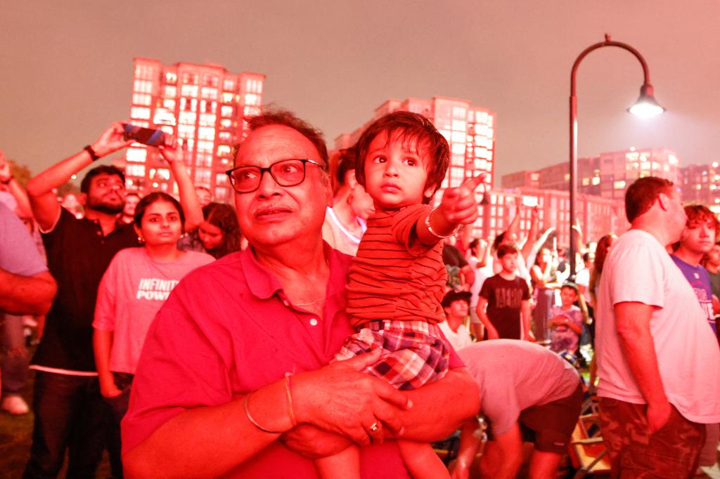 A man holds a child as people stand on the banks of the Hudson River to watch the annual Macy's Independence Day fireworks show in Hoboken, New Jersey, on July 4, 2024.