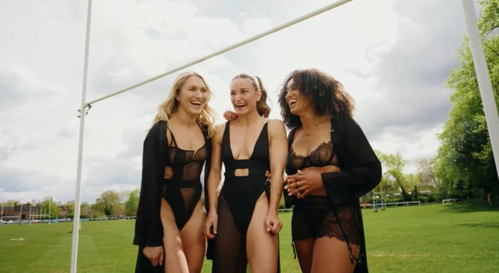 Professional female rugby players from Team GB in black lingerie on a pitch, participating in a 'strong is beautiful' campaign