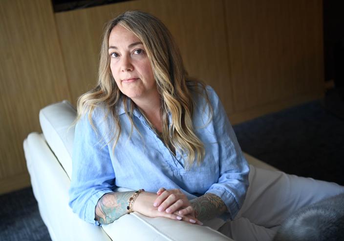 alisha price, seen here with long blonde hair looking into the camera, leaning on the arm of a chair while wearing a powder blue top and light colored pants