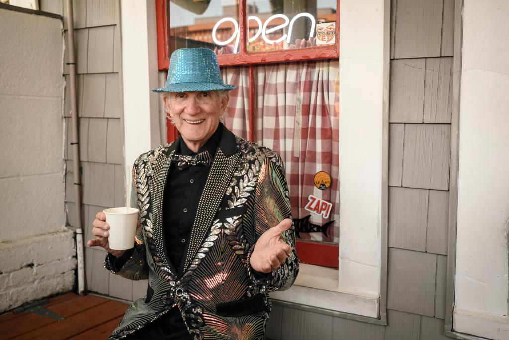Owen Loof, identified as the best-dressed man in Rockaway, at Connolly's bar, holding a cup and wearing a hat and jacket