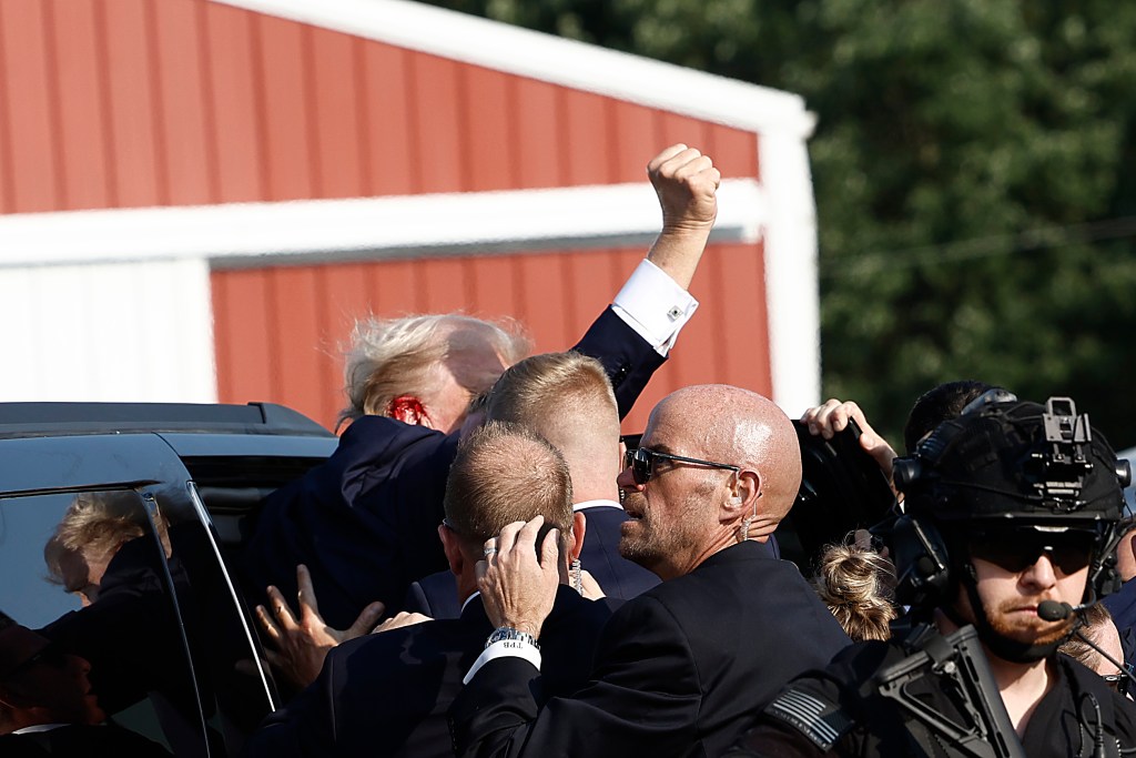 Trump raising his fist to the crowd as he is rushed into a vehicle after the shooting.