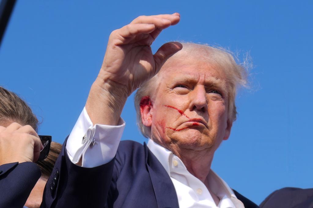 Former President Donald Trump waving from the stage surrounded by Secret Service agents at a campaign rally in Butler, PA, 2024