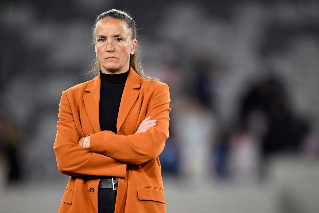 San Diego Wave FC head coach, Casey Stoney, in an orange jacket with her arms crossed, looking on after a match at Snapdragon Stadium.