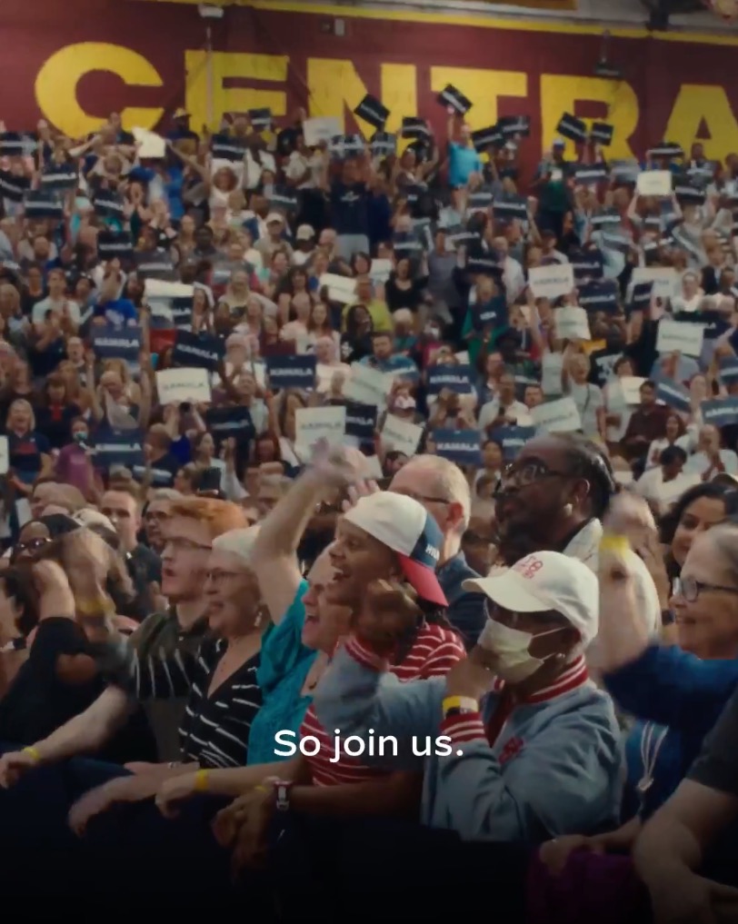 The ad shows rally goers holding Harris signs.