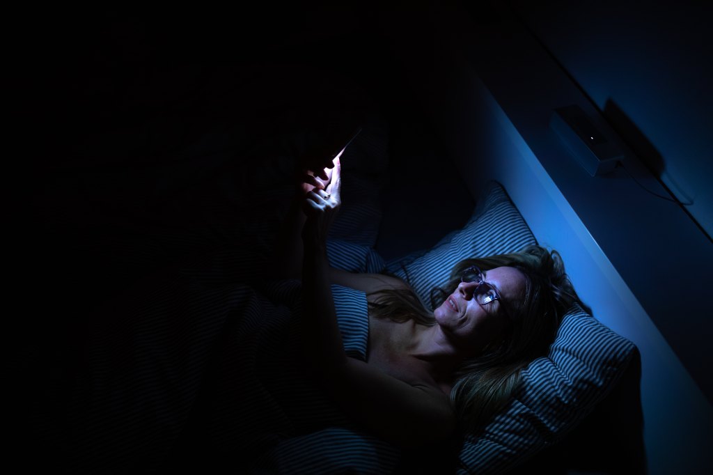 STOCK Pretty, middle-aged woman using her cell phone in bed at night - unhealthy blue light exposure