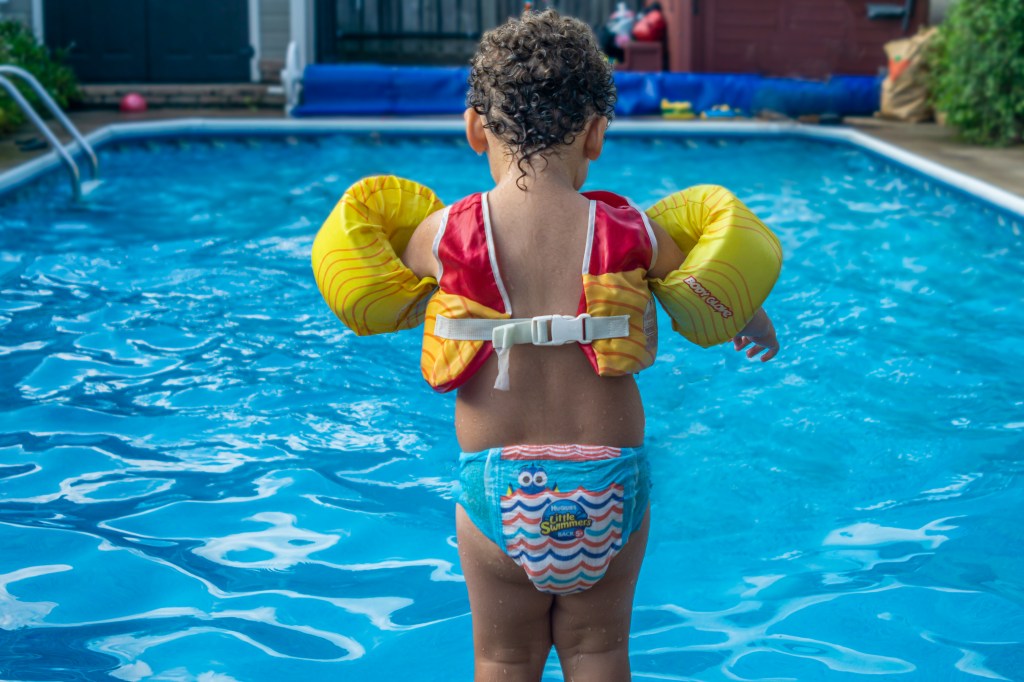 Toronto, Canada, August 2020 - Toddler boy in water wings stands at edge of swimming pool ready to jump into water; Shutterstock ID 1959382843; purchase_order: -; job: -; client: -; other: -