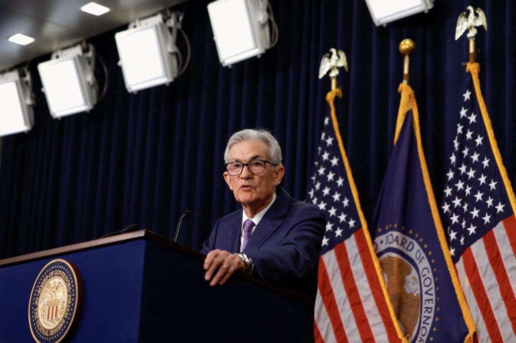 U.S. Federal Reserve Chair Jerome Powell standing at a podium with flags behind him, delivering remarks during a press conference