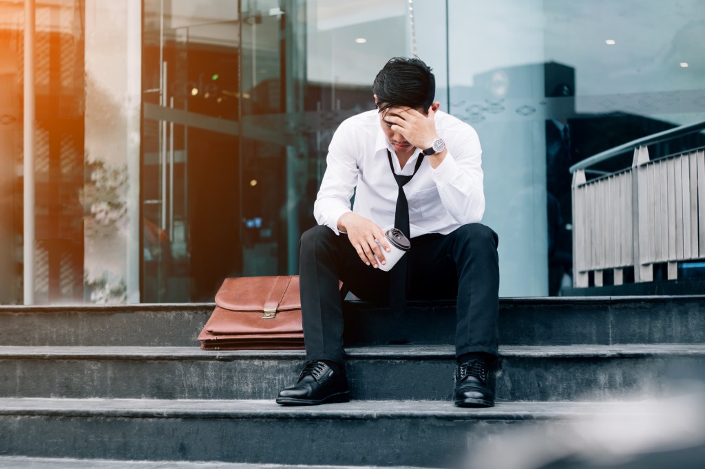 Distressed businessman sitting on steps with his hand on his head in a concept of unemployment