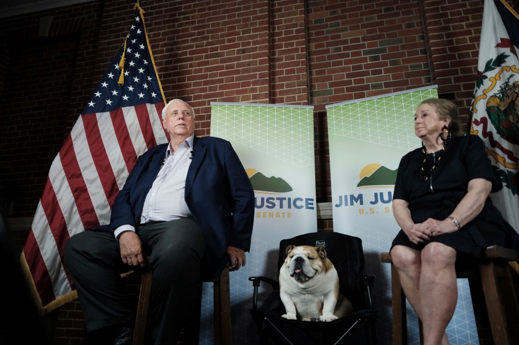 West Virginia Governor Jim Justice speaking at an election watch party, with his wife Kathy and dog Babdog listening attentively