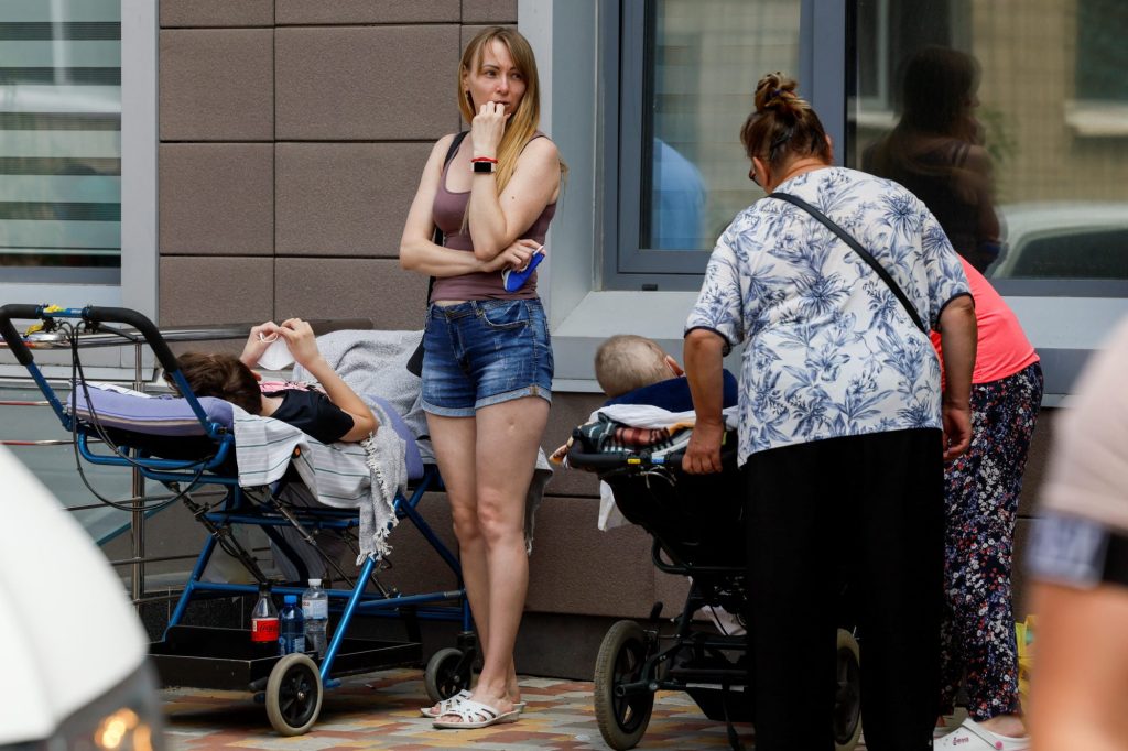 A woman stands next to patients near Ohmatdyt Children's Hospital that was damaged during Russian missile strikes.