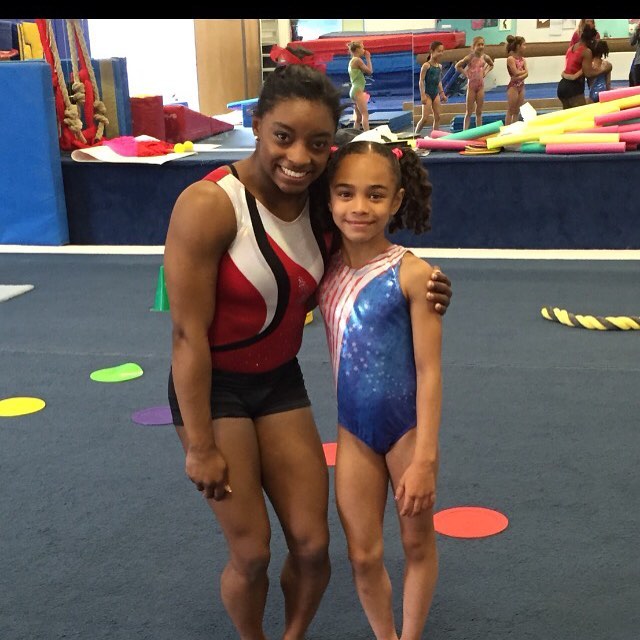 Simone Biles posing affectionately with a young girl at the gym