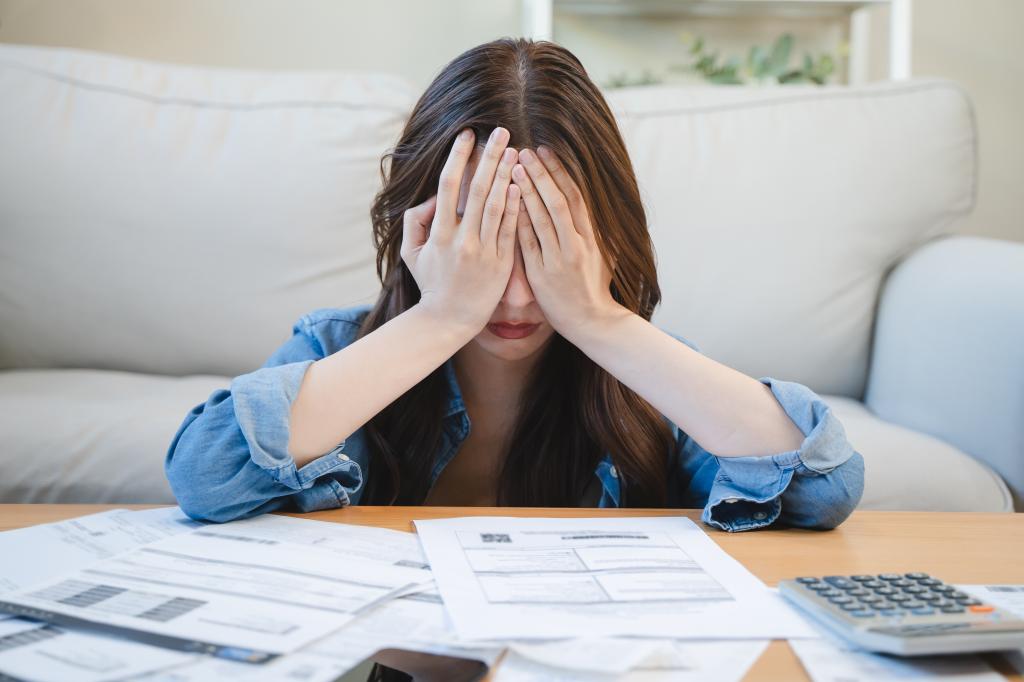 Young Asian woman covering her head with her hands, stressed over monthly bill expenses and credit card debt