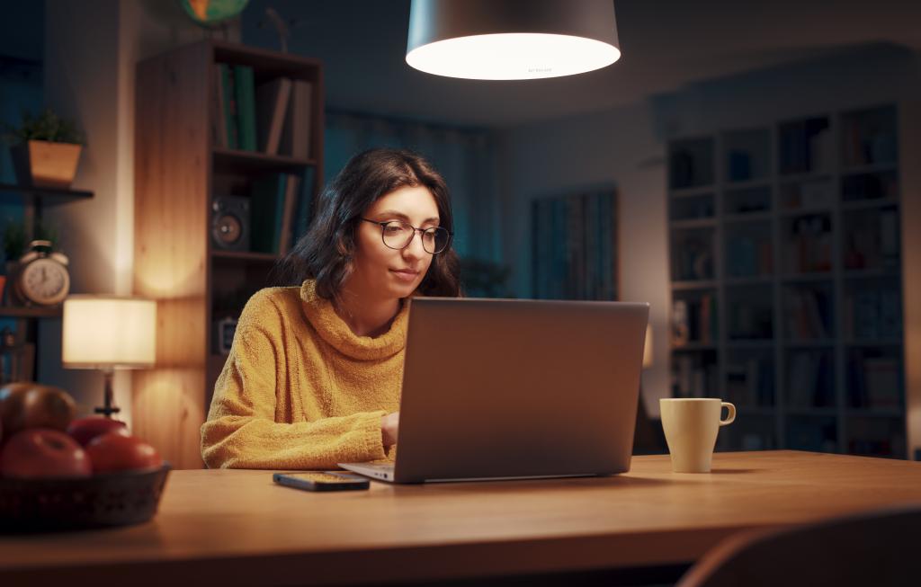 Young woman sitting at her desk at night and connecting with her laptop, online learning and social media concept