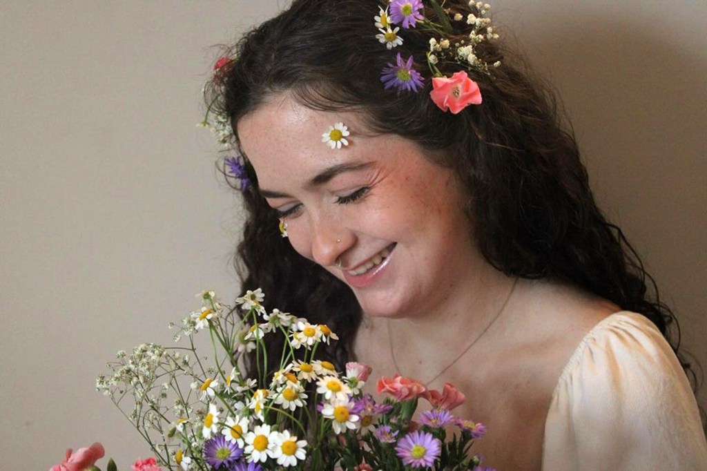 Young woman with flowers in her hair and holding a colorful bouquet of wildflowers, identified as Autumn McClure, who tragically passed away in a car accident